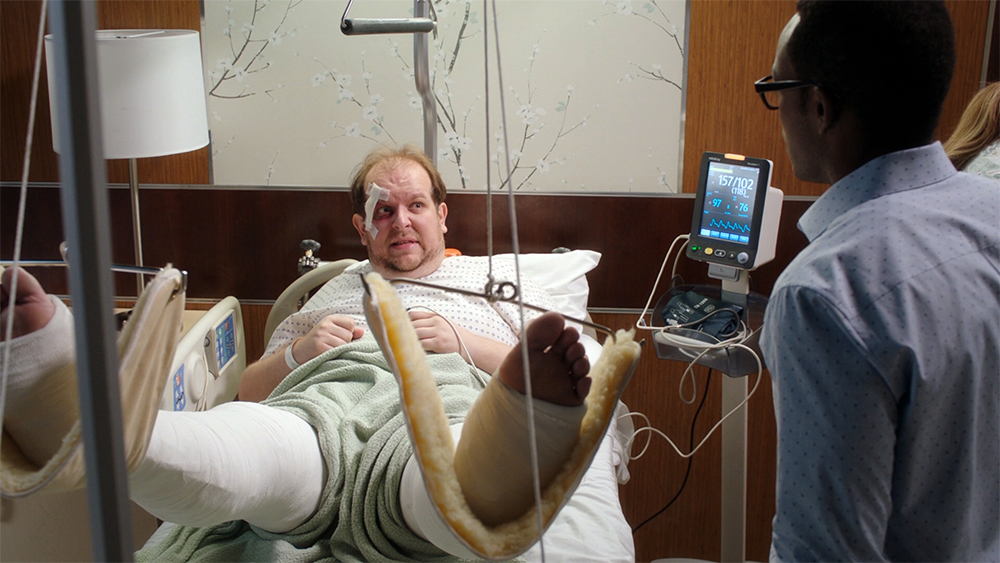 Man in a hospital bed is visited by a friend.