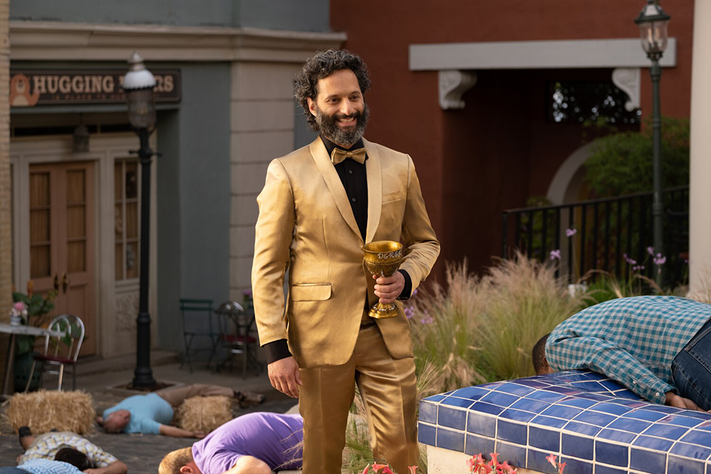 A man in a golden suit walks down the street with a golden challice.