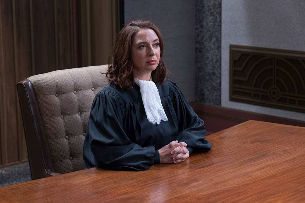 Fun fact: She likes to binge-watch TV! A judge sits solemnly at a table.
